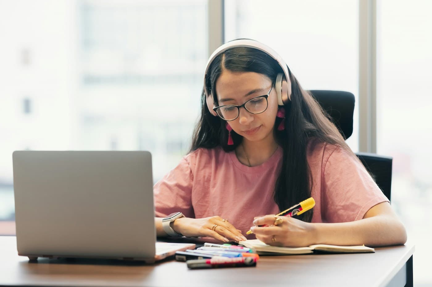 Người học đeo tai nghe và viết ghi chú bên máy tính.